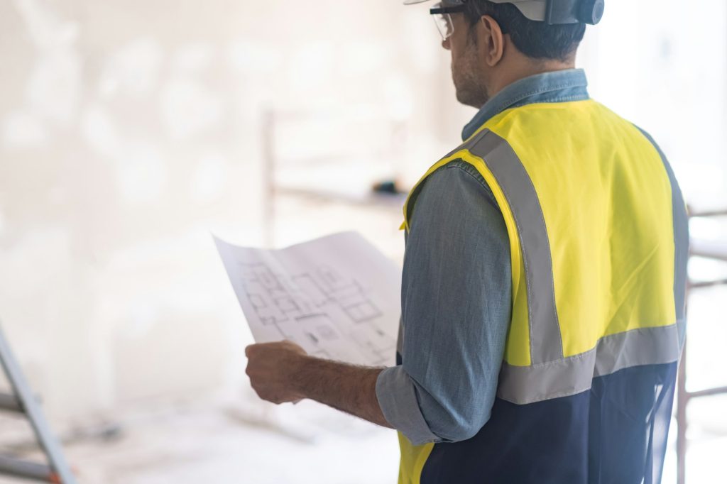 Experienced worker in professional uniform checking condition of wall in room